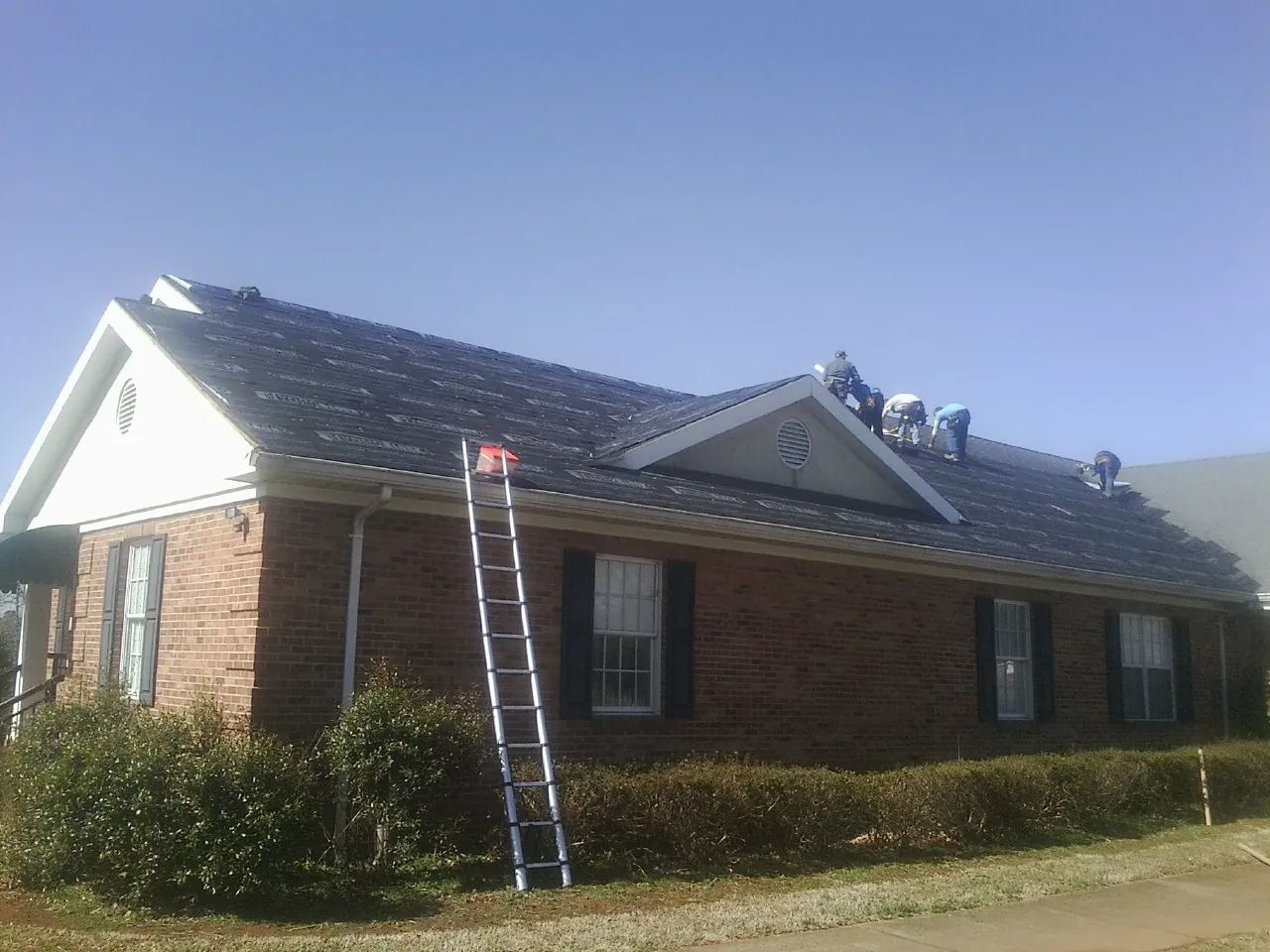 Crew tearing shingles off a brick ranch roof with a ladder set — Metal Roof Repair work by our crew in Linwood