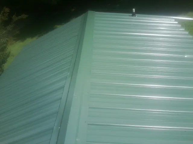 New green metal panels meeting at the ridge of a roof — Flat Roof Repair work by our crew in Linwood