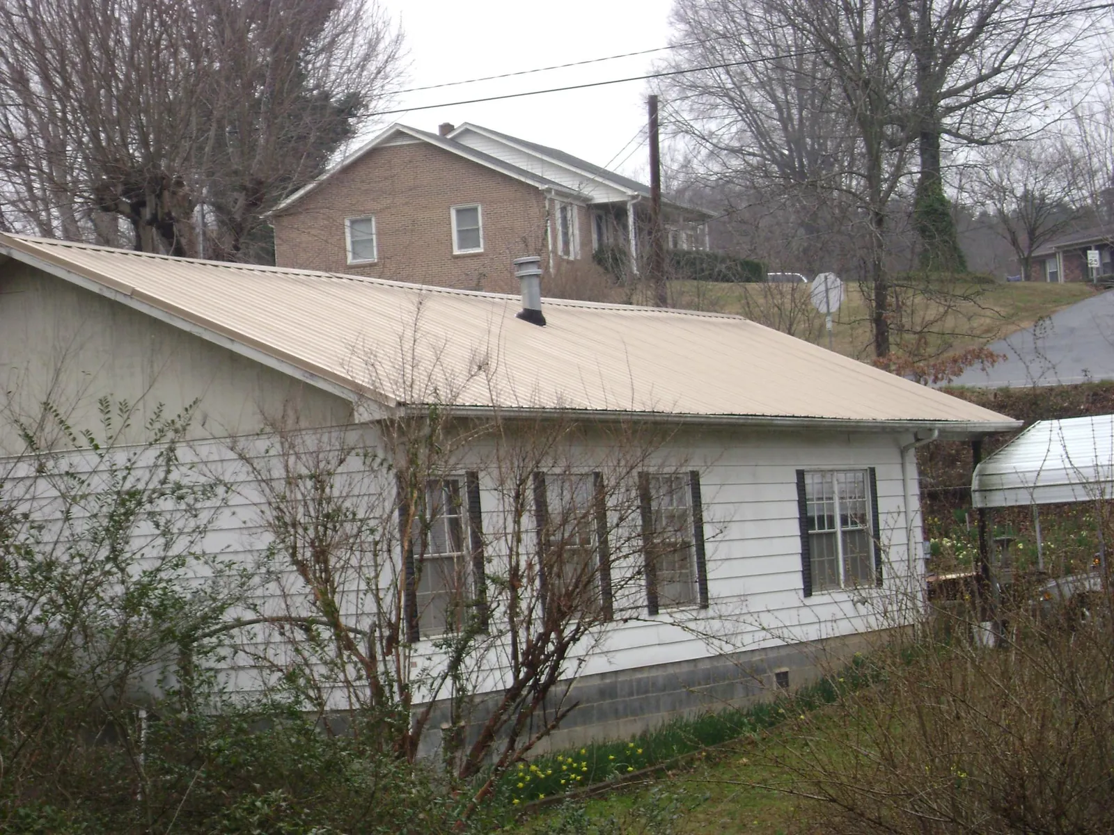 Tan metal roof on a white sided house set into a hillside — Commercial Roofing by Roofing Brothers in Linwood
